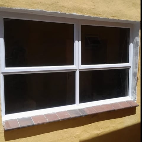 Empty storefront window with white frame divided into four sections, dark interior, and brick sill