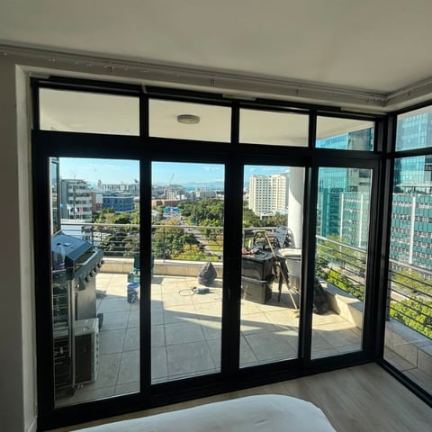 Modern black-framed sliding glass doors opening to a high-rise urban balcony with city skyline and mountains visible in the distance