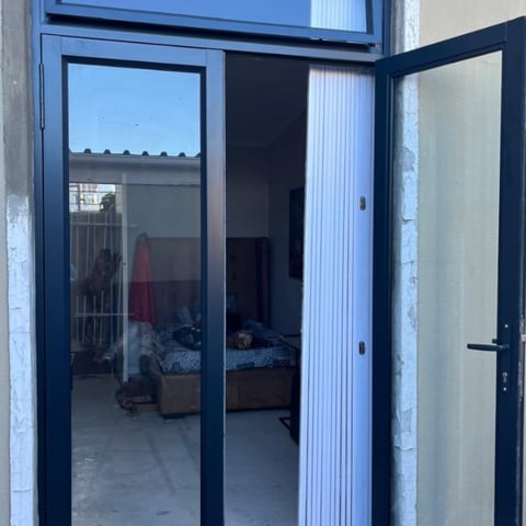 Navy blue modern glass doors and frame opening into a bedroom with bed and furnishings visible inside