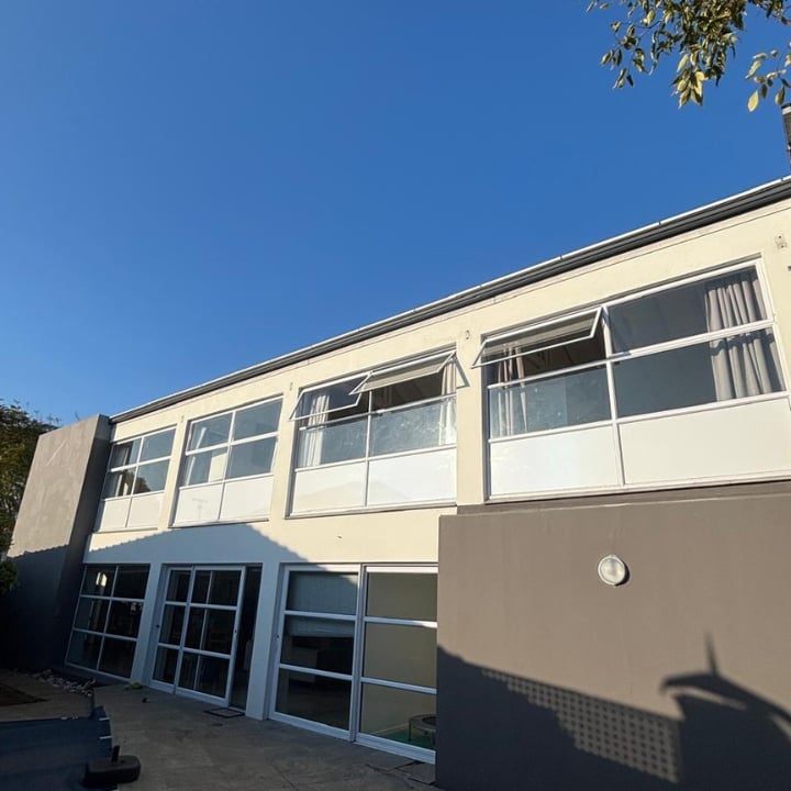 Modern two-story building with cream and blue facade, large windows, and clear blue sky overhead.