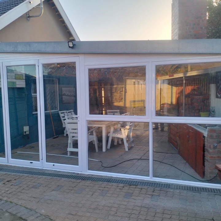 Modern glass and white frame patio extension with interior seating visible through windows on a brick paved surface