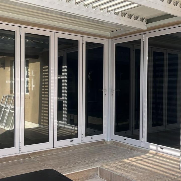 Modern white aluminium bi-fold doors open onto a wooden patio with pergola overhead