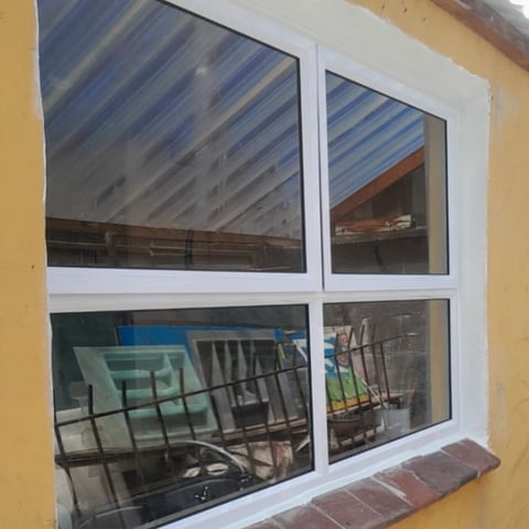 White-framed window with four panes on yellow wall, showing reflected interior construction and scaffolding