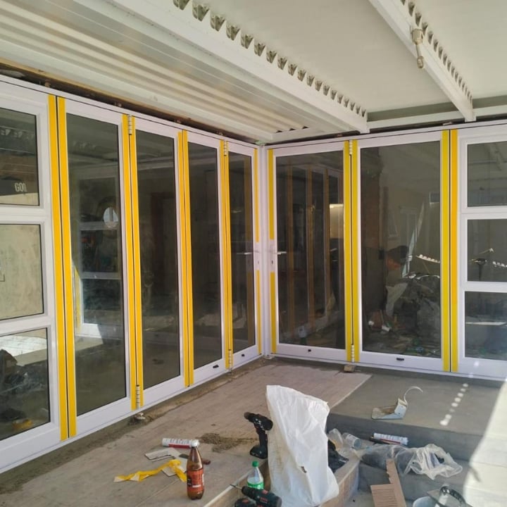 Large yellow and white bifold glass doors being installed in a residential interior with construction materials on the floor