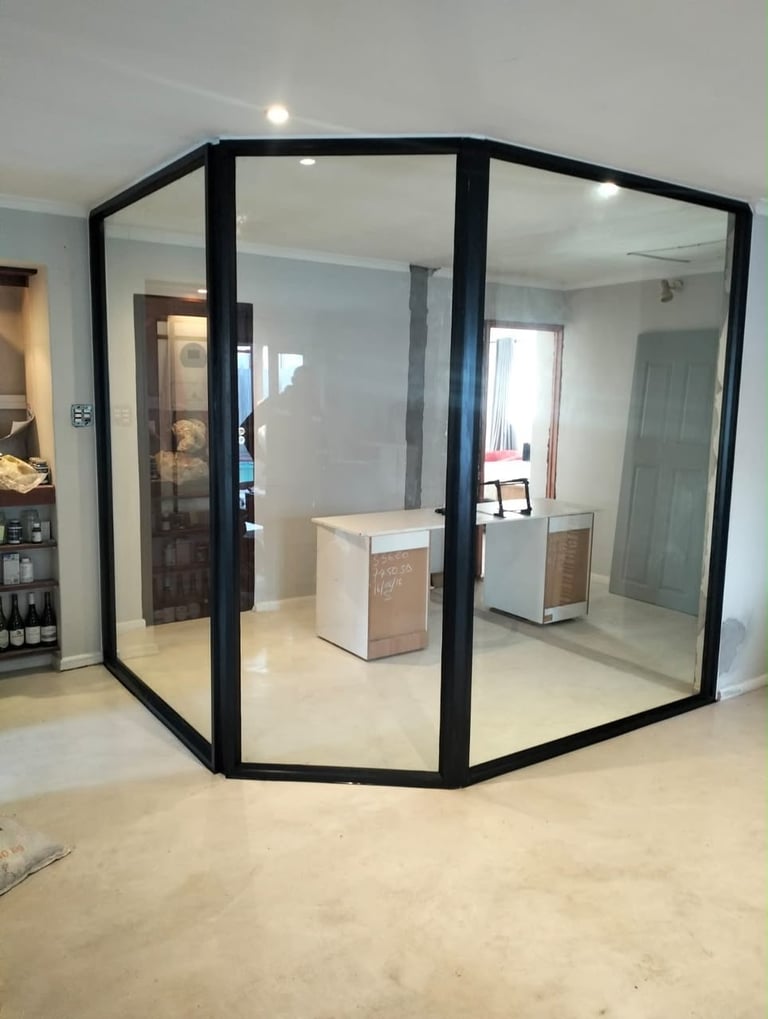 Modern black-framed glass enclosure with white cabinetry inside, installed in a residential interior space with polished concrete floor.