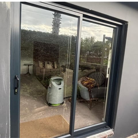 Black framed glass patio doors opening to a garden patio with a white compost bin and garden furniture visible outside