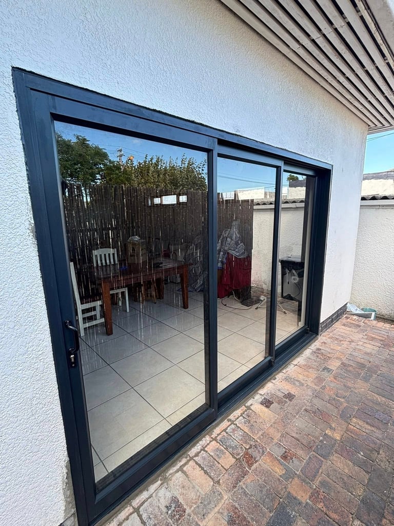 Modern black-framed glass sliding doors opening onto a patio with red chairs and potted plants