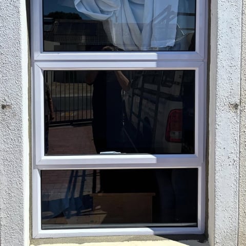 Three-pane white-framed window on white wall showing interior reflections and shadows