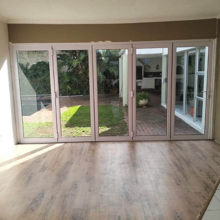 Empty room with wood-look flooring and multi-panel glass sliding doors opening to a patio and backyard garden