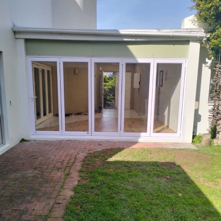 Modern white house with multi-panel sliding glass doors opening to a brick patio and manicured lawn.