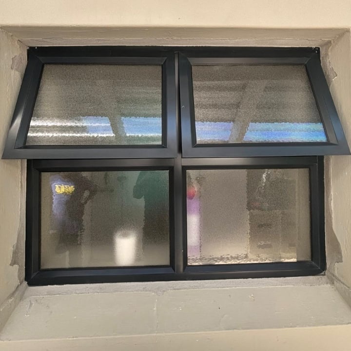 Four-pane window with black frames in cream-colored wall, showing blue sky reflection in upper panes and interior view in lower panes