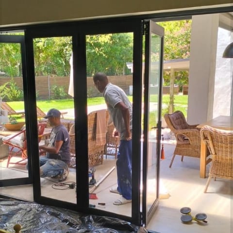 Two people working on installing new black-framed glass doors in a home with garden view