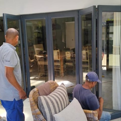 Two workers installing large dark-framed sliding glass doors on a residential patio entrance
