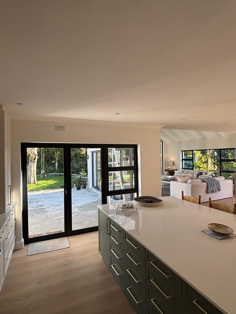 Modern open-plan kitchen and living area with black framed glass doors opening to a patio and green yard
