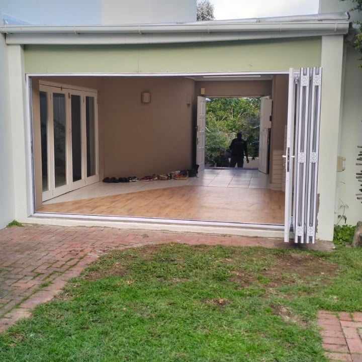 Open garage with wooden floor, white frame doors, brick patio, and green lawn in front