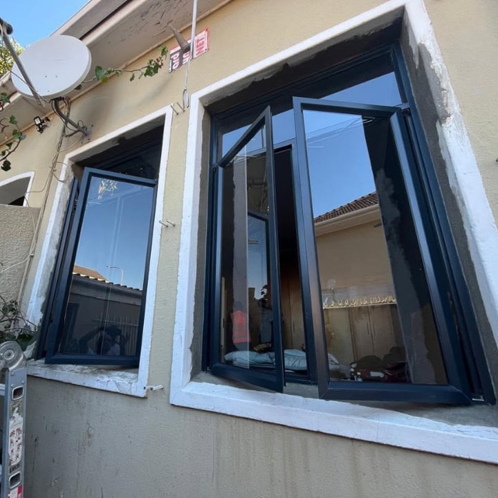 Two black-framed windows with white trim installed on a light-colored residential building exterior