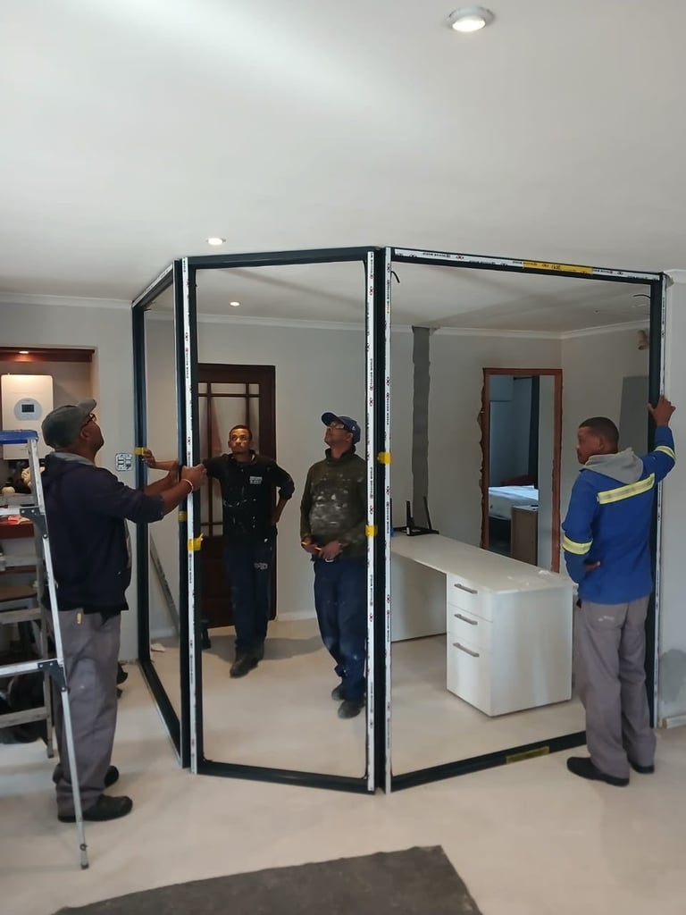 Workers installing a large black-framed glass room divider or partition wall in an interior space